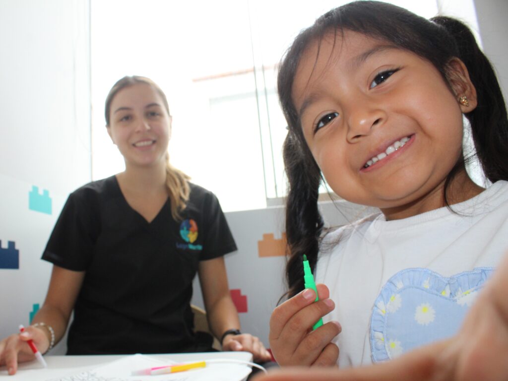 Niña sonriendo durante una sesión terapéutica mientras una terapeuta acompaña el trabajo en mesa en LegoMente.