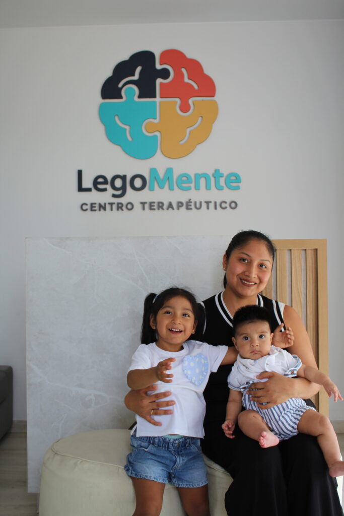 Madre con sus dos hijos en la recepción de LegoMente, frente al logo del centro terapéutico.