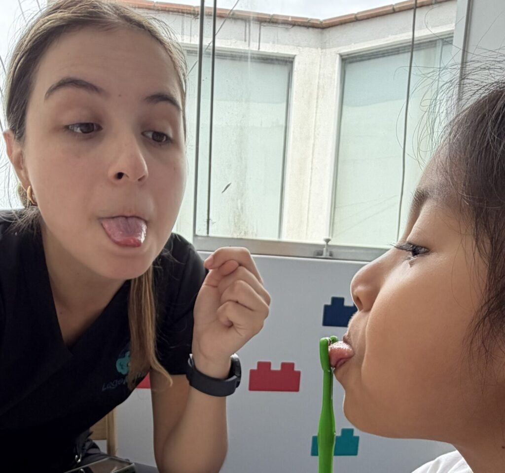 Terapeuta de lenguaje guiando a una niña en un ejercicio de motricidad oral con apoyo visual en LegoMente.