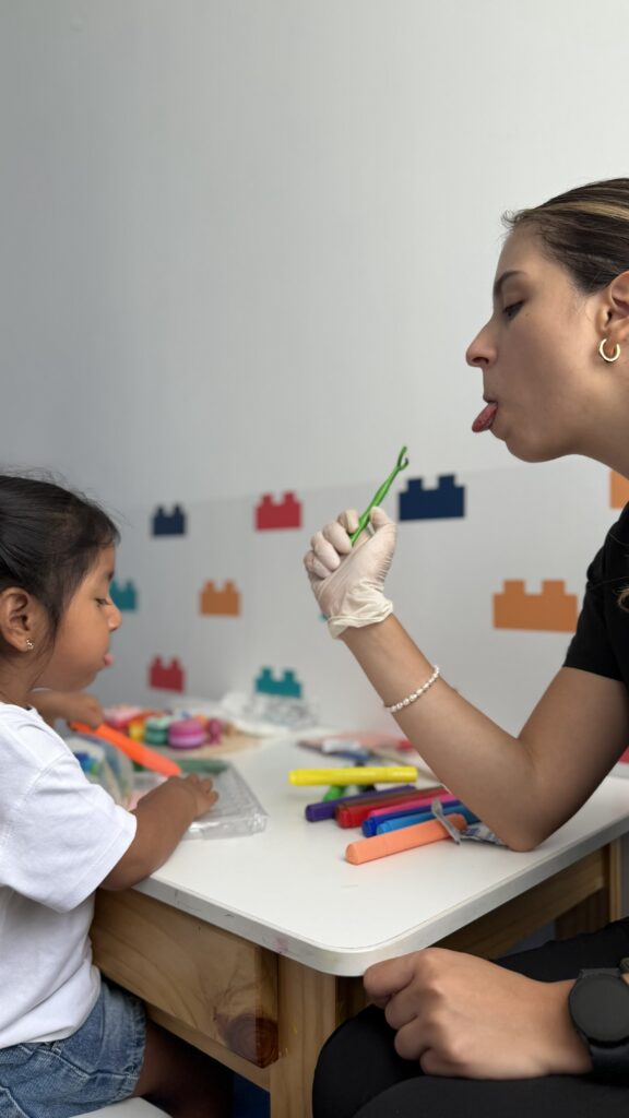 Terapeuta de lenguaje realizando un ejercicio de imitación oral con una niña durante una sesión en LegoMente.